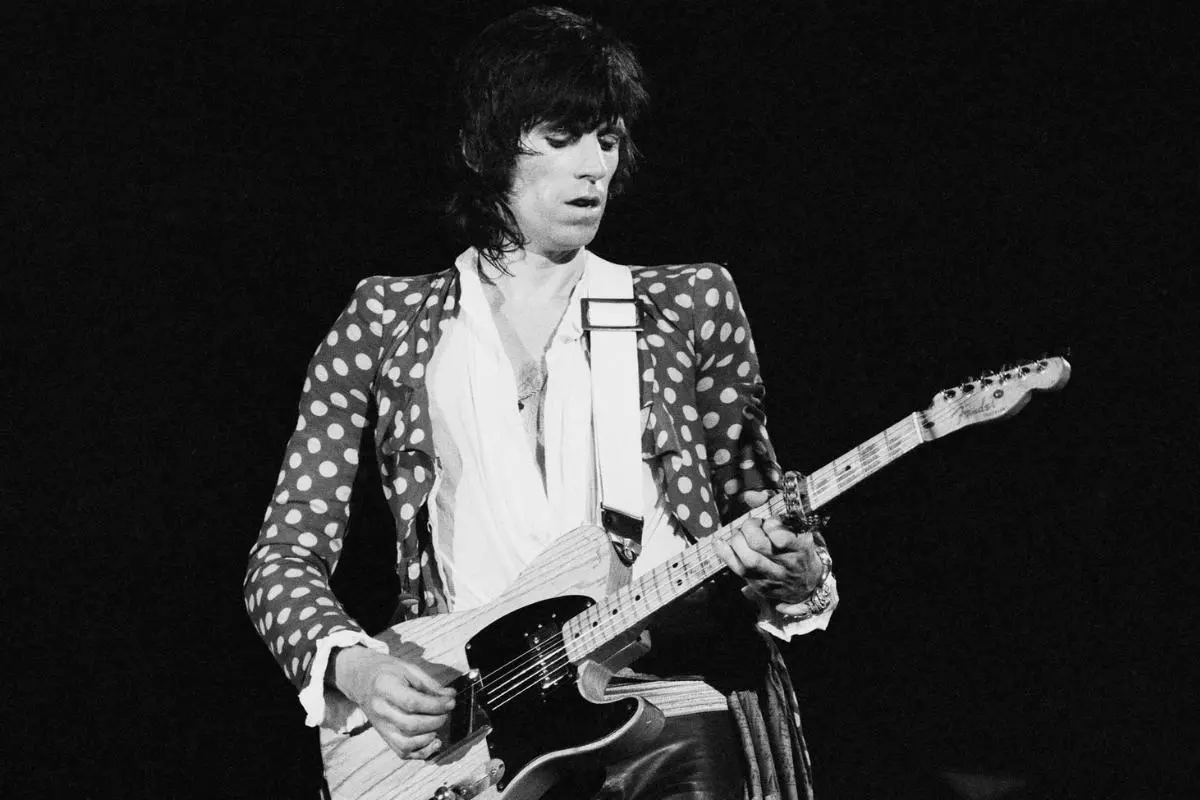 Keith Richards playing an electric guitar on stage in a polka-dot jacket.
