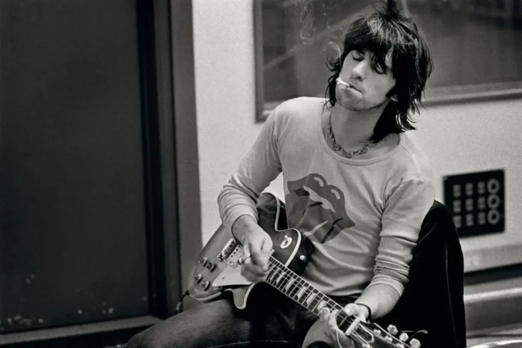 Keith Richards seated indoors playing guitar during a rehearsal.
