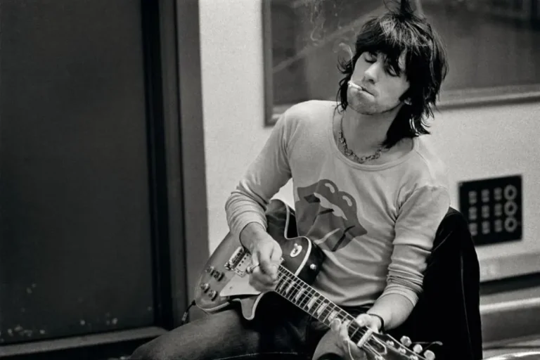 Keith Richards seated indoors playing guitar during a rehearsal.