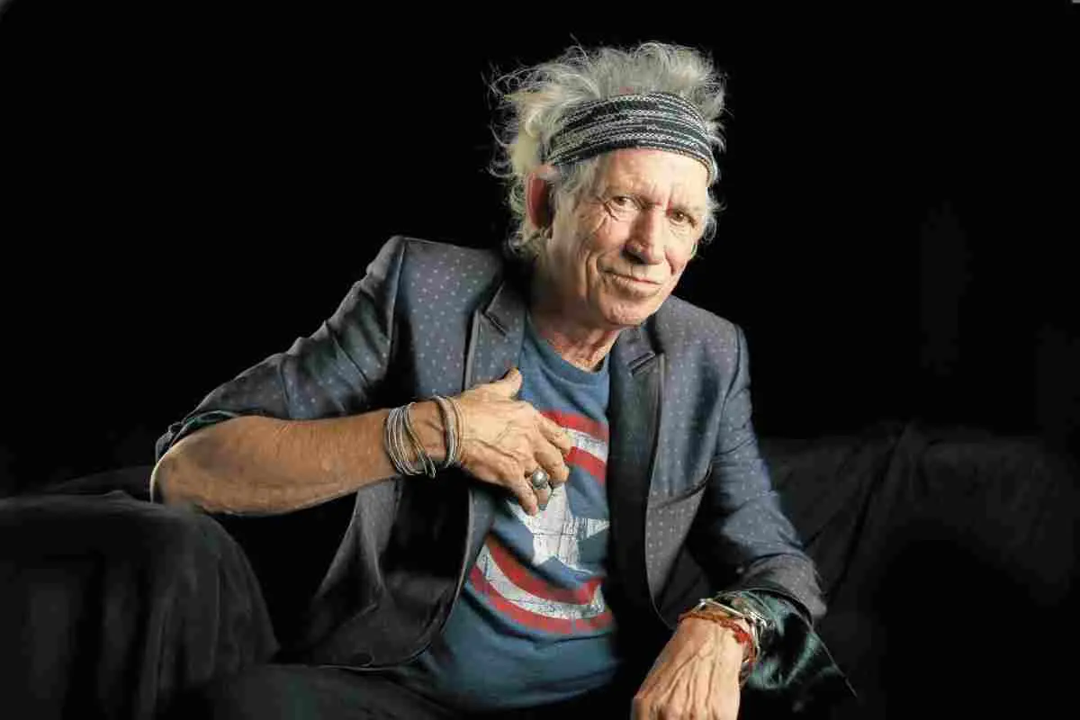 Keith Richards sitting in a studio setting, wearing a blazer and headband.