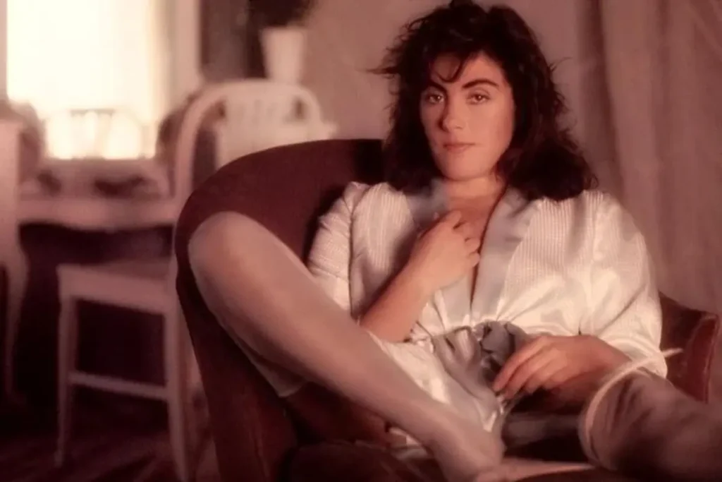 Laura Branigan reclining in an armchair in a softly lit studio portrait, wearing a light robe and tights, looking calmly toward the camera in an intimate, early-career photo.