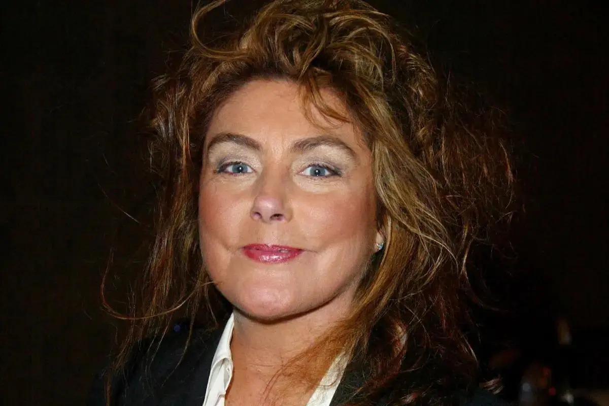 Laura Branigan posing in a close-up portrait, smiling gently toward the camera, with voluminous hair and natural makeup against a dark background.