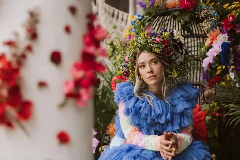 Lauren Daigle seated wearing a floral crown and blue ruffled dress in an artistic portrait setting.