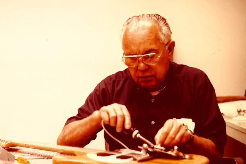 Leo Fender working at a bench, adjusting guitar electronics by hand.