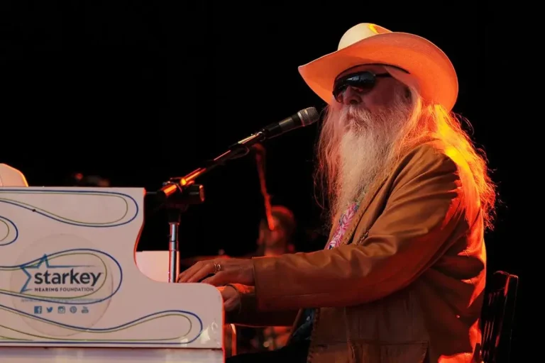 Leon Russell performing at a piano onstage, wearing a cowboy hat and sunglasses.
