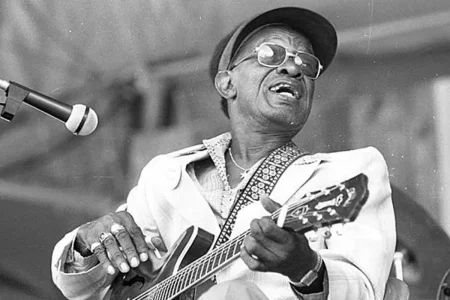 Lightnin Hopkins singing while playing an electric guitar on stage, capturing the energy and emotion of a live blues performance.