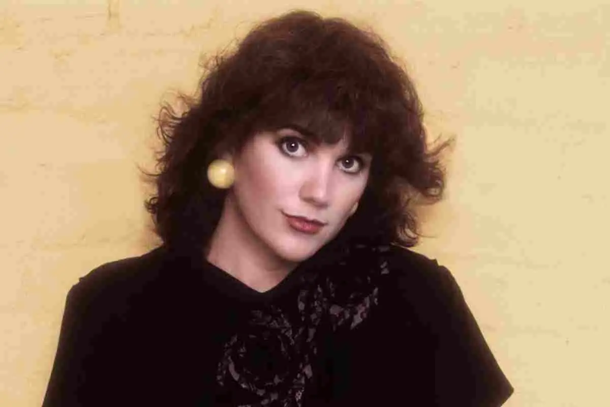Linda Ronstadt posing in a studio portrait, wearing a dark top and large earrings.