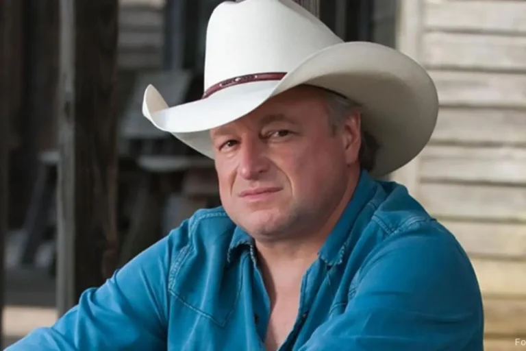 Mark Chesnutt sitting outdoors wearing a white cowboy hat and blue button-down shirt, looking directly at the camera with a calm, reflective expression.