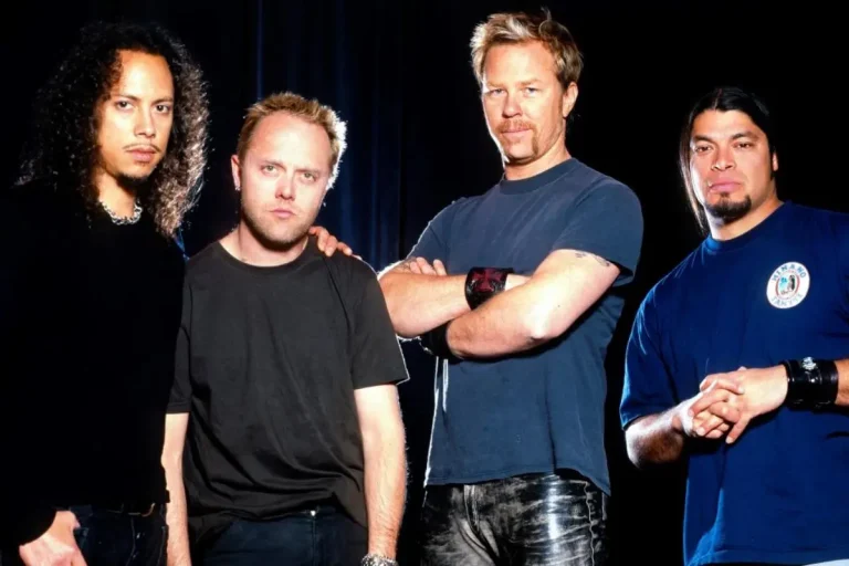 Four-piece metal band poses onstage with arms crossed under dramatic lighting.