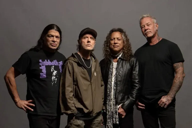 The Metallica band stand together for a studio portrait, dressed in casual dark clothing, looking directly at the camera.