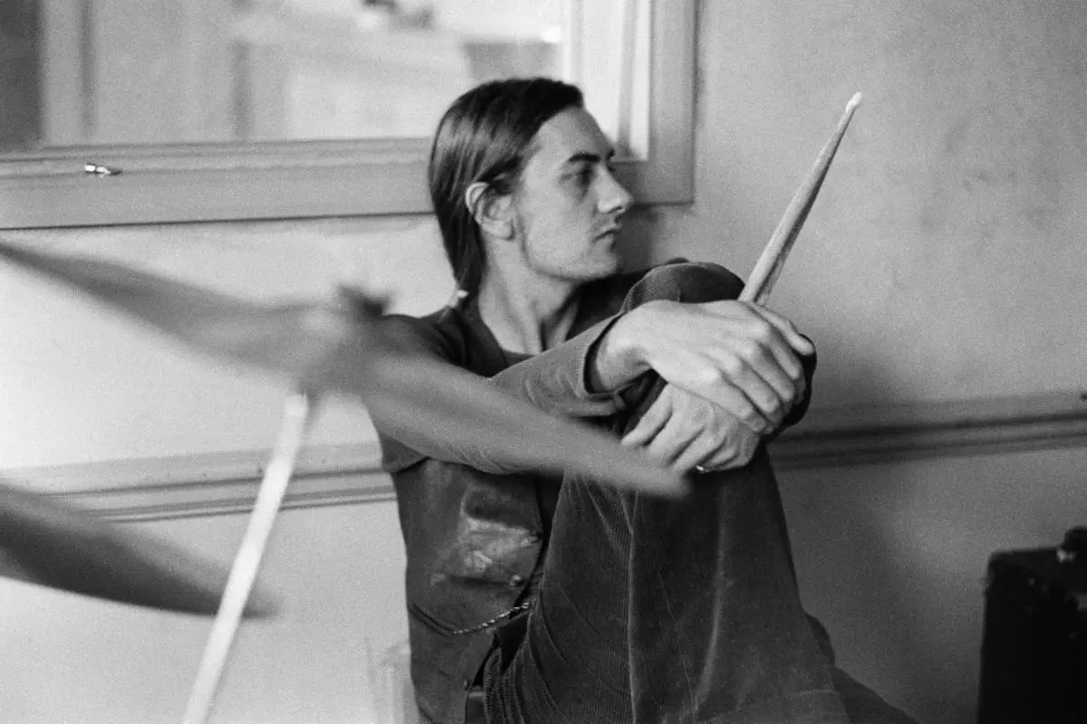 Mick Fleetwood seated indoors holding drumsticks in a black-and-white photo.
