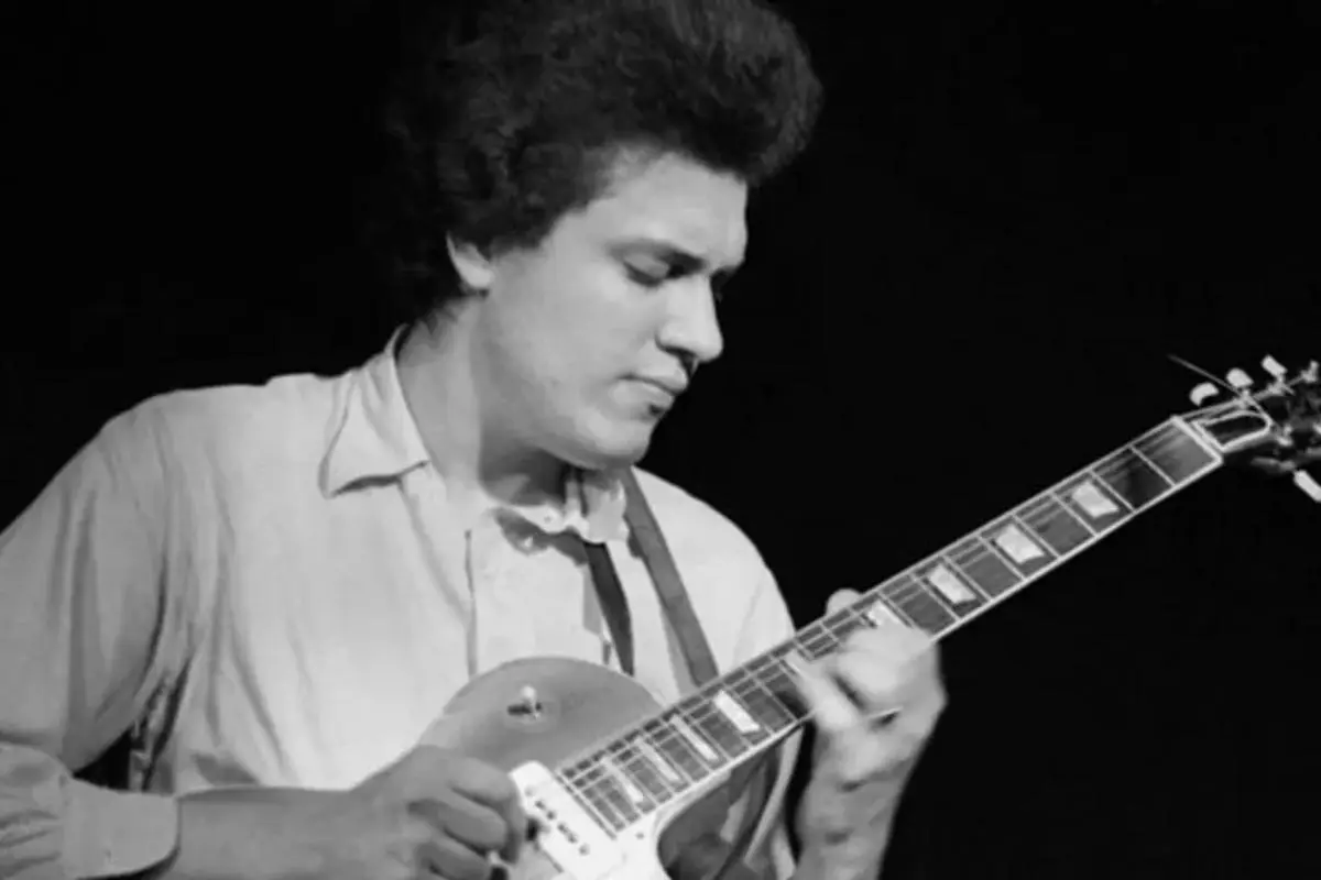 Mike Bloomfield playing an electric guitar in a black-and-white performance photo, focused intently on the fretboard, wearing a light-colored shirt against a dark stage background.