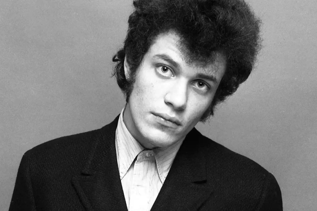 Mike Bloomfield posing in a black-and-white studio portrait, wearing a dark jacket over a buttoned shirt, looking directly at the camera with a serious expression.