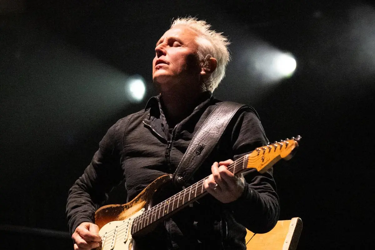Mike McCready performing live on stage, playing electric guitar under dramatic concert lighting.