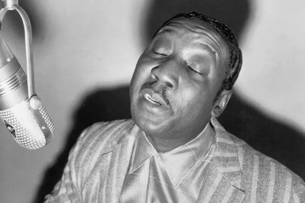 Black-and-white portrait of Muddy Waters singing into a studio microphone with eyes closed.