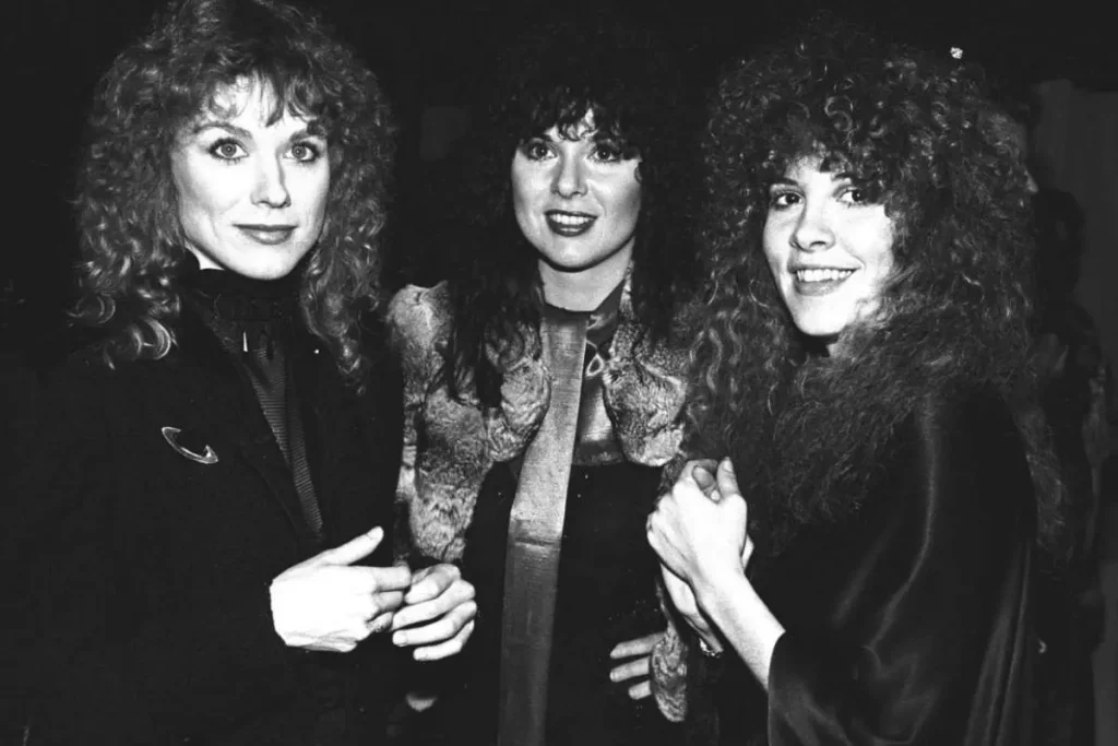 Nancy, Ann Wilson and Stevie Nicks stand together at an event, dressed in dark, textured clothing, smiling and looking toward the camera in a candid group moment.