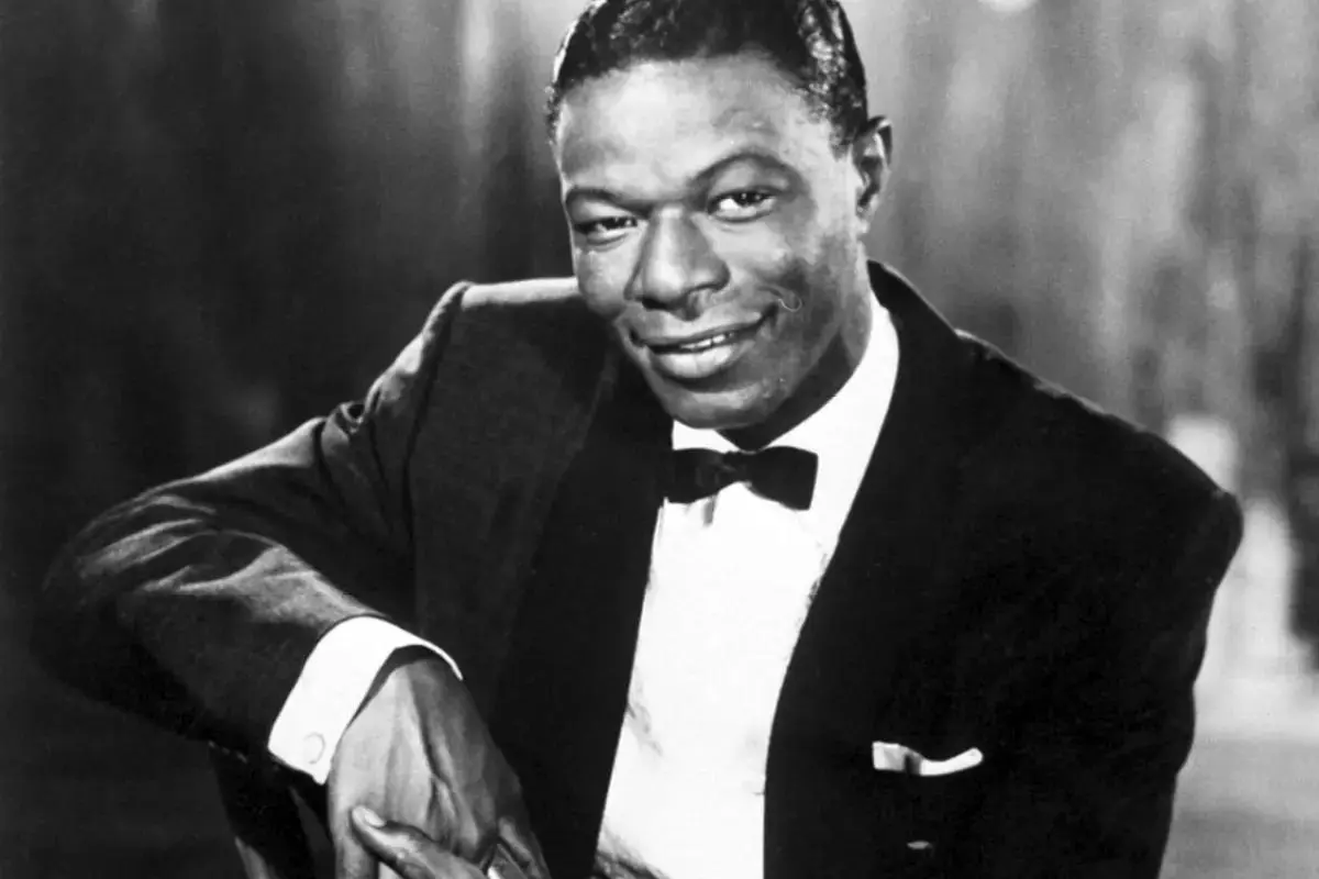Nat King Cole in a tuxedo and bow tie, leaning on his arm with a warm, relaxed smile.