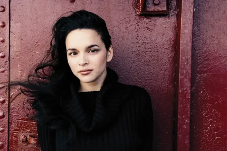 Norah Jones with dark hair swept back, wearing a black top.