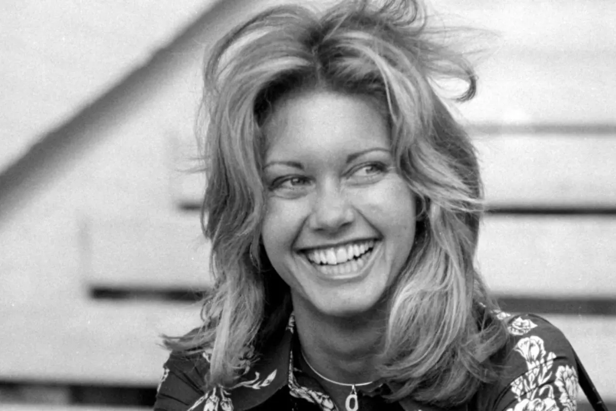 Olivia Newton laughing openly outdoors, capturing warmth, approachability, and a relaxed, natural expression.