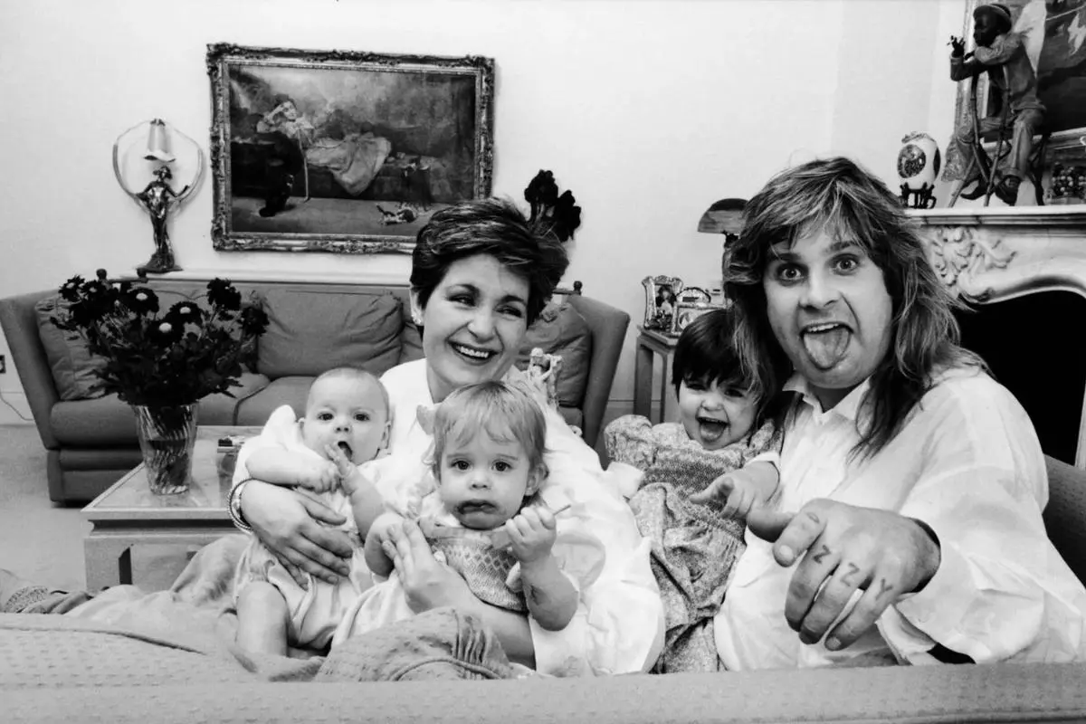 Ozzy and Sharon seated on a sofa holding babies and smiling.