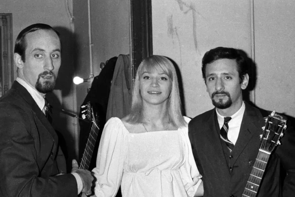 Peter, Paul and Mary standing together indoors, conveying collaboration, simplicity, and the intimacy of early acoustic music culture.