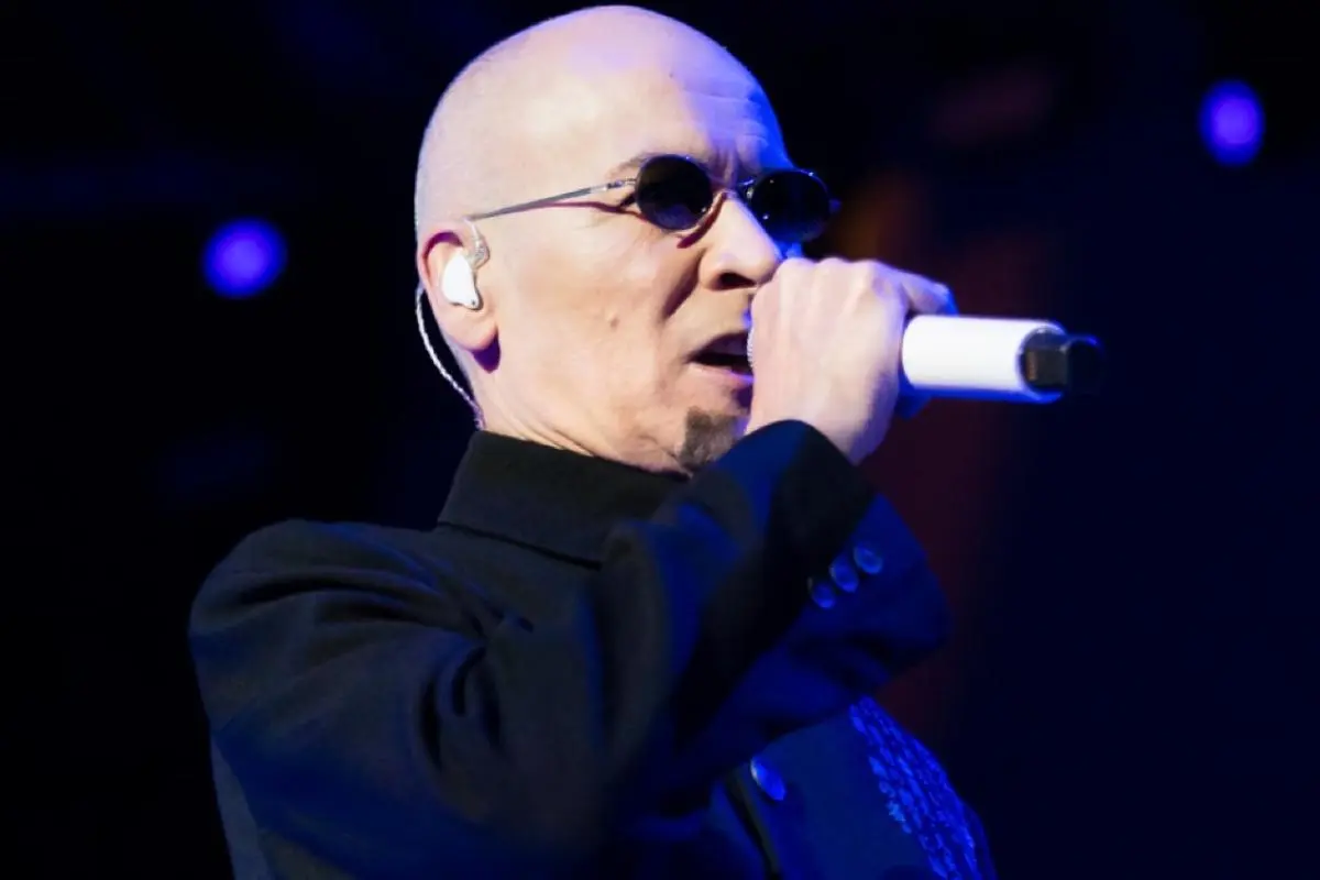 Phil Oakey of The Human League performs onstage wearing dark sunglasses.