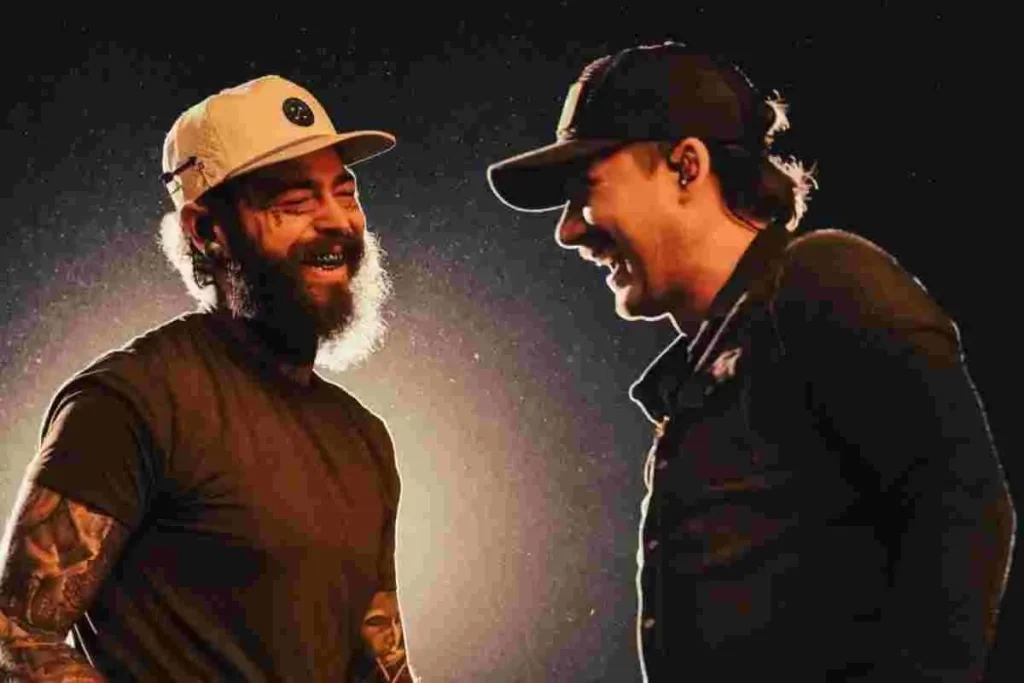 Post Malone and Morgan Wallen laughing together backstage, facing each other in casual hats and dark clothing.