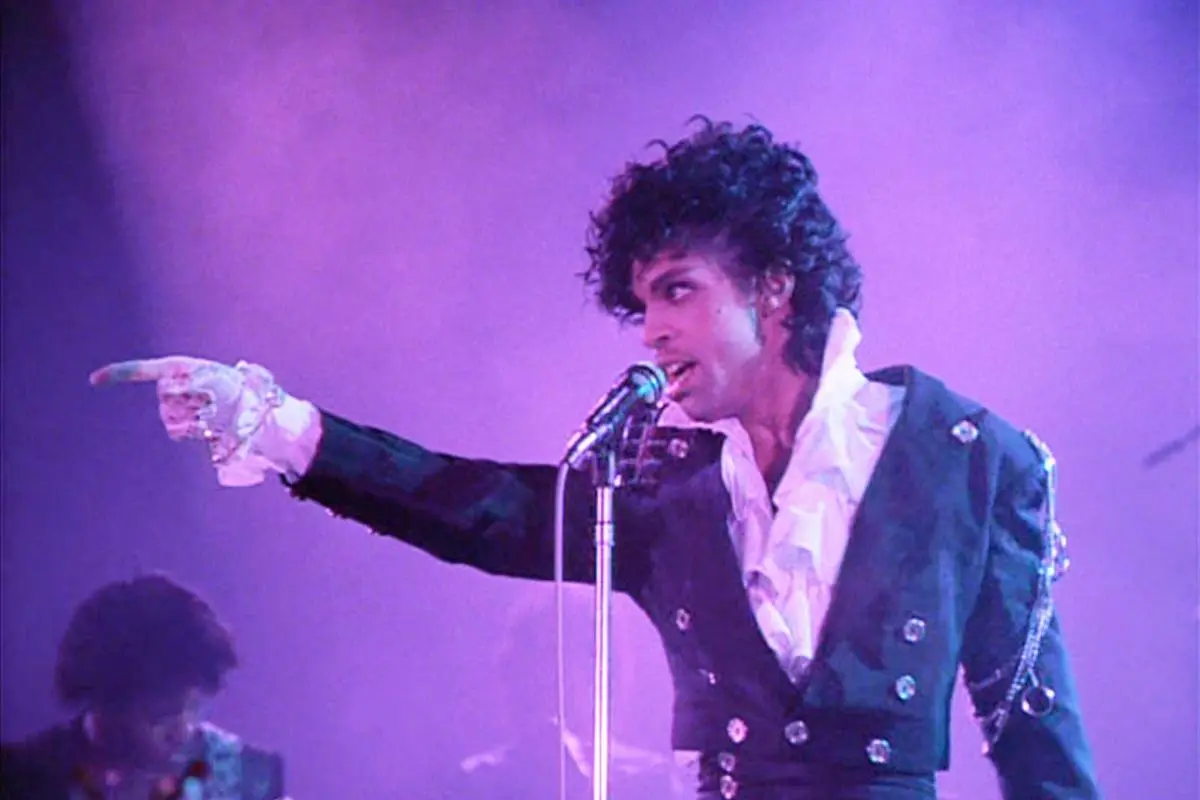 Prince pointing toward the audience while singing into a microphone.
