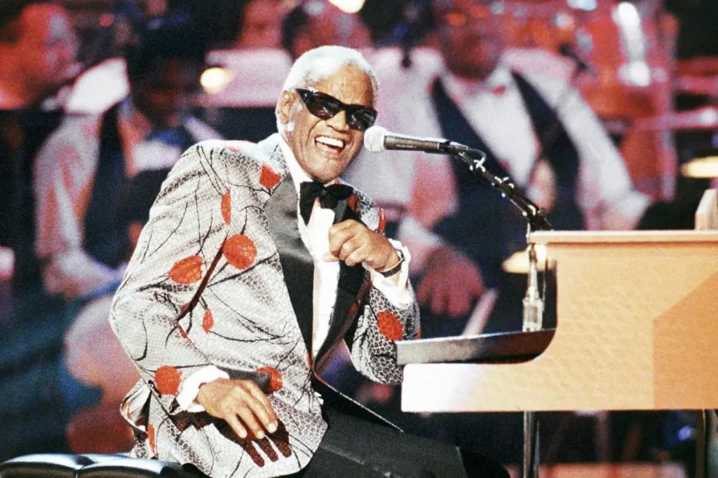 Ray Charles Wasn’t “In” Music – Music Was Him: The Blues Seasoning That Changed Everything Ray Charles in a patterned jacket and sunglasses, seated at a piano during a live performance.