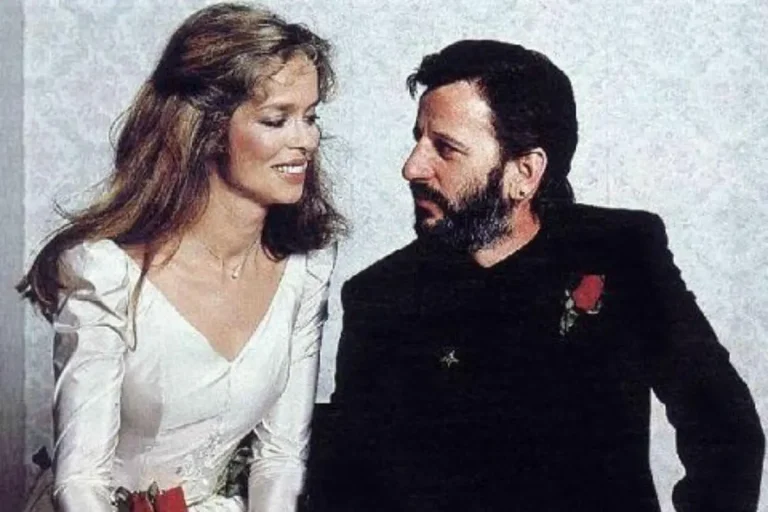 Ringo Starr’s Two Weddings: From Beatlemania Backlash to 80s Redemption A Ringgo"s wedding in a white dress sit close together, smiling warmly at each other with red rose boutonnieres pinned to their outfits.