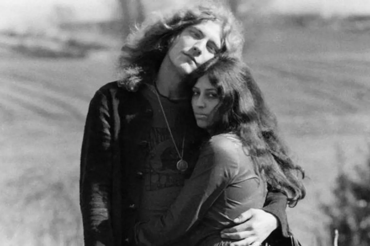 Robert and his wife Maureen embrace outdoors, standing close together with a serene landscape in the background.