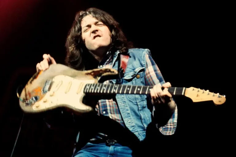 Rory Gallagher performing live with an electric guitar under stage lights.