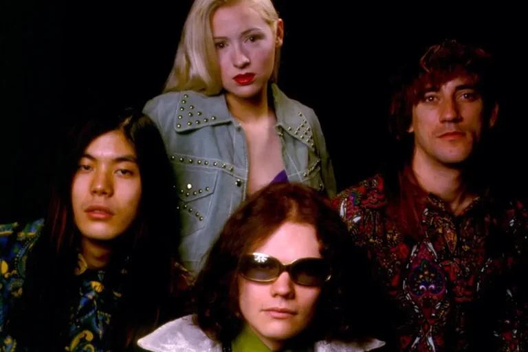 The Smashing Pumpkins band portrait with four members in patterned outfits against a dark background.