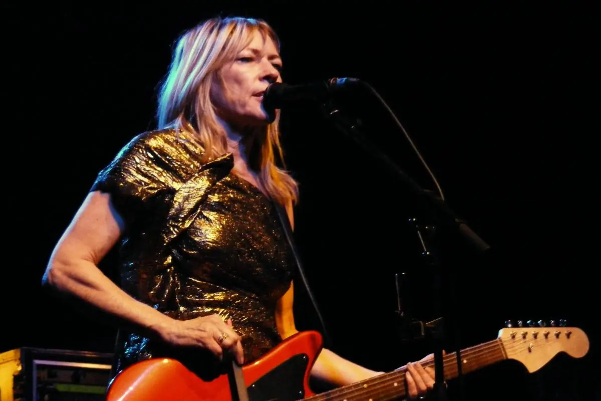 Sonic member performs onstage singing into a microphone while playing an electric guitar under dark concert lighting.