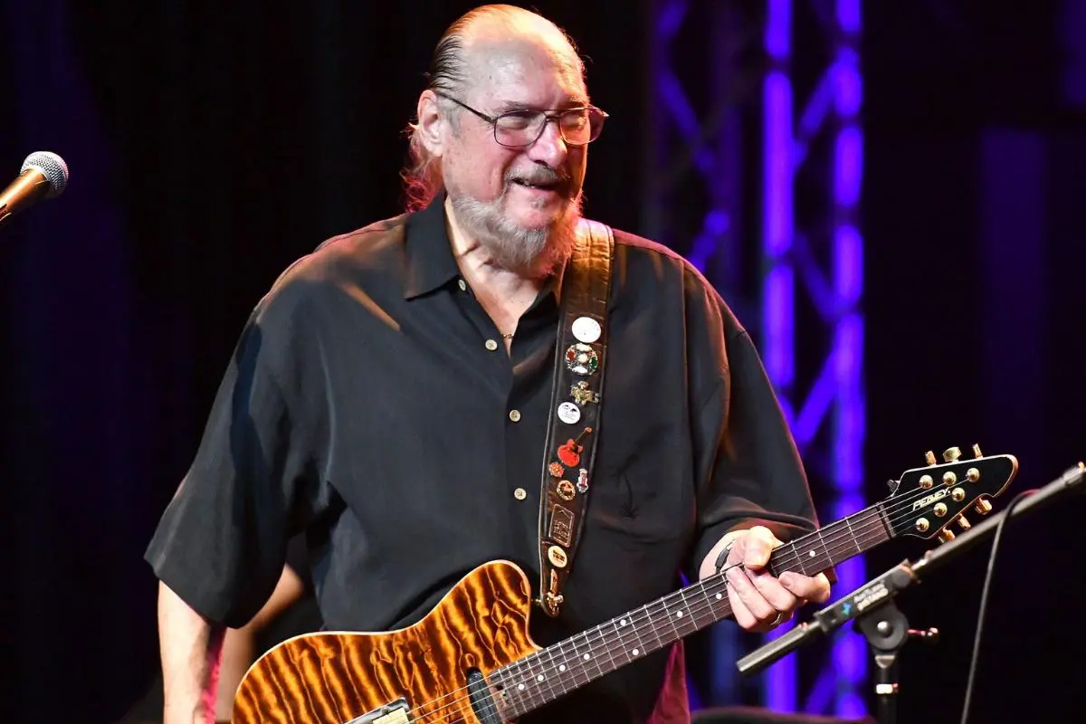 Steve Miller smiles onstage while playing an electric guitar with a tiger-stripe finish.