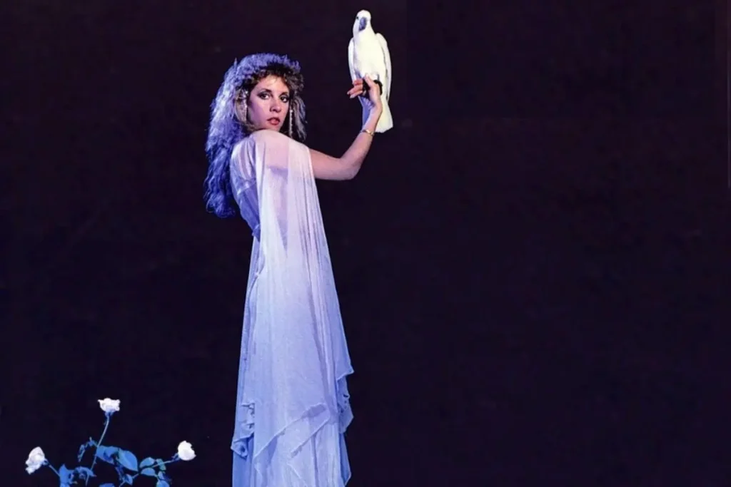 Stevie Nicks holding a white dove onstage in a flowing white dress.