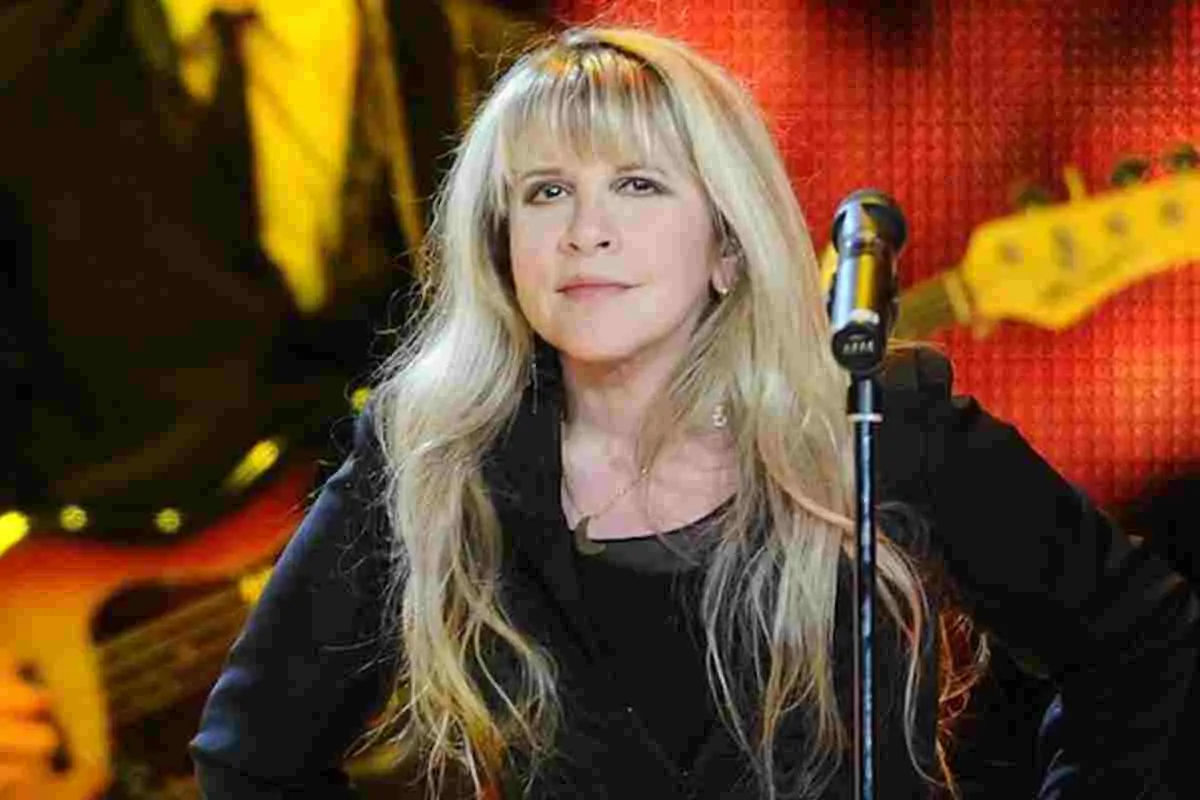 Stevie Nicks standing on stage behind a microphone, blonde hair and black outfit.