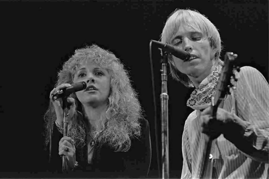 Stevie Nicks and Tom Petty performing together on stage, singing into microphones.