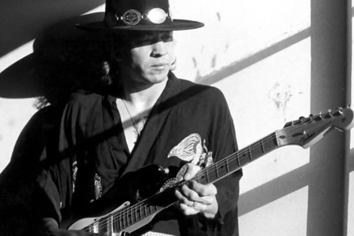 Black-and-white photo of Stevie Ray Vaughan playing electric guitar under dramatic lighting.