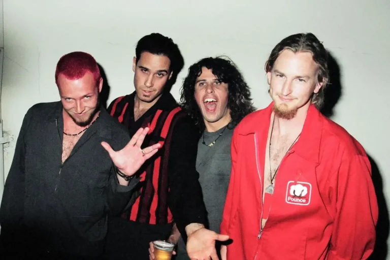 Stone Temple Pilots standing together indoors, dressed in dark and red clothing with playful expressions.