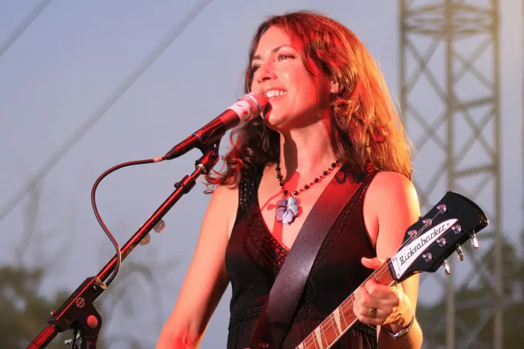 Susanna Hoffs performs onstage, singing into a microphone while playing an electric guitar.