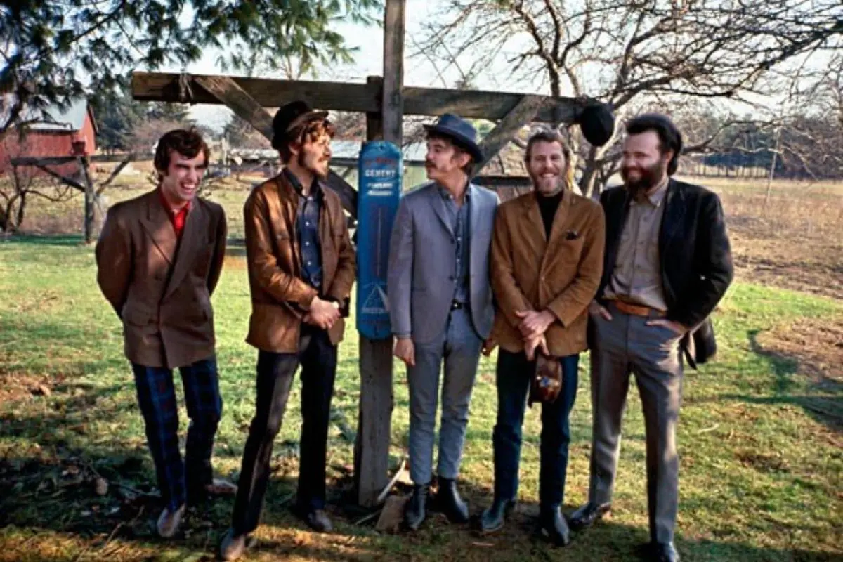 The Band standing together outdoors near a wooden fence in casual vintage attire.