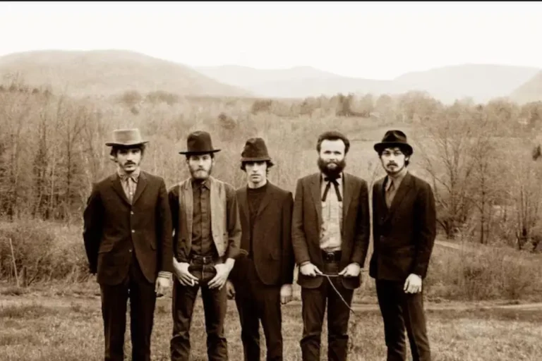 The Band posing outdoors in vintage suits with a rural landscape in the background.