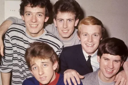 The Hollies, five smiling band members gathered closely together indoors.