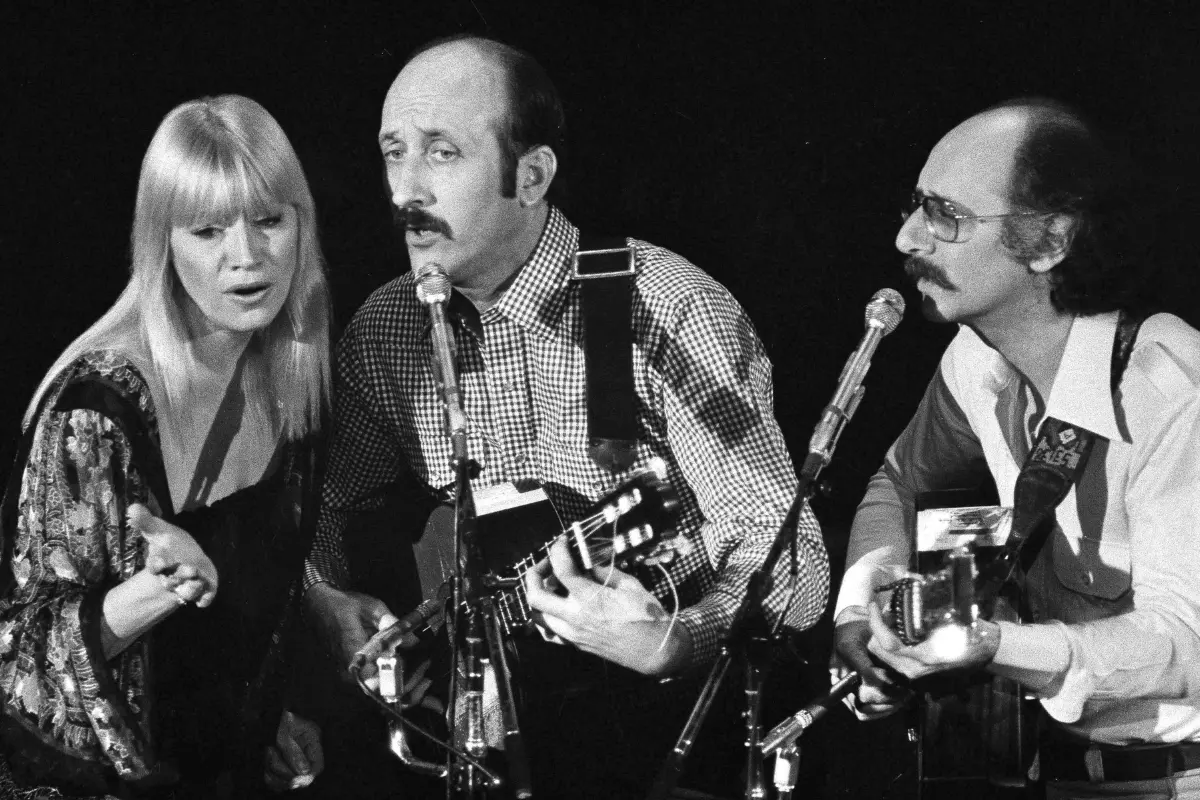 Peter Paul and Mary performing together on stage with acoustic guitars and shared microphones, emphasizing harmony, storytelling, and collective performance.