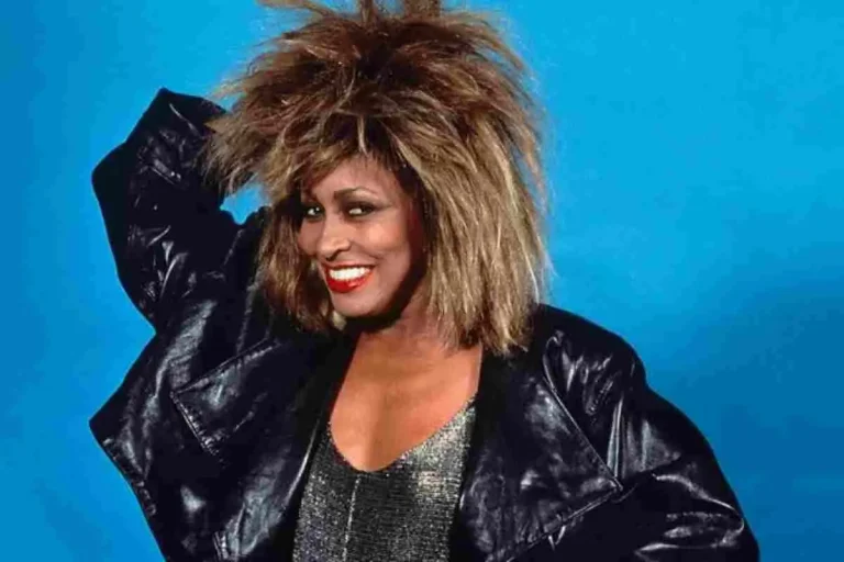 Tina Turner smiling in a studio portrait, wearing a black jacket with voluminous hair.