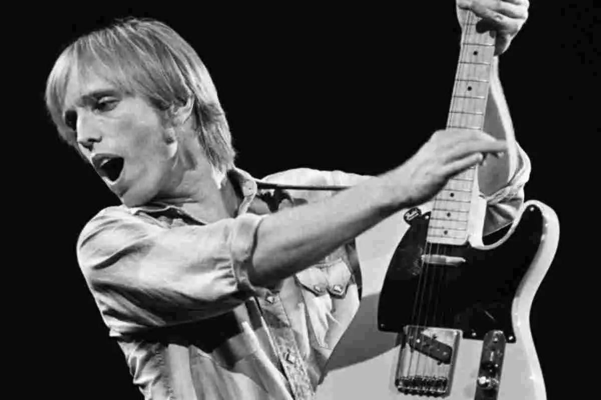 Tom Petty playing electric guitar on stage in a black-and-white performance photo.