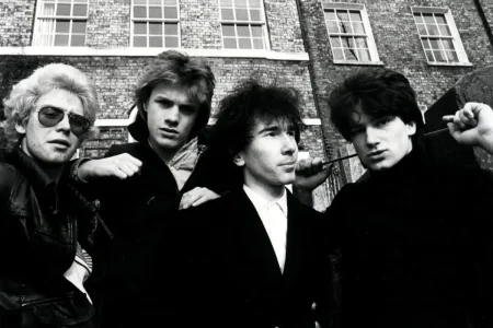 U2 band members outdoors, posing closely with intense expressions in front of brick buildings.