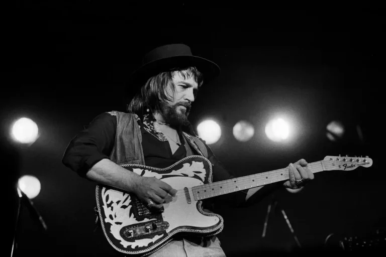 Waylon Jennings playing a custom Telecaster guitar on stage.
