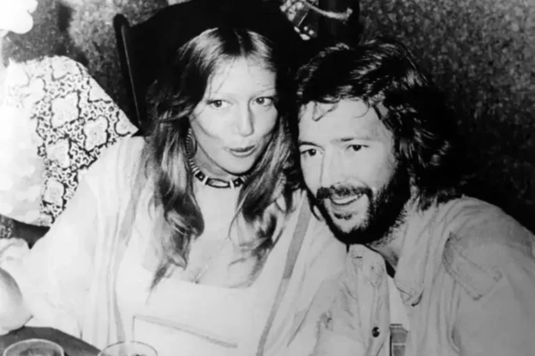 Eric Clapton and Pattie sits closely at a table, smiling and talking in a dimly lit setting.